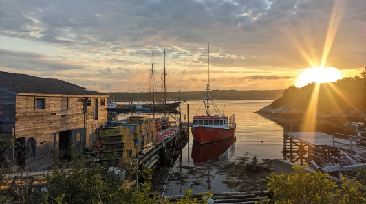 A boat at a dock, with the sun setting over calm waters 